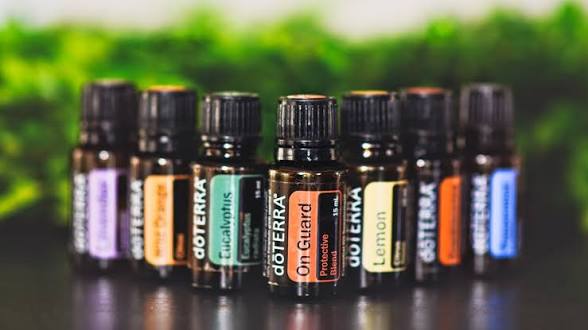 Fila di flaconi dōTERRA, tra cui Eucalyptus, On Guard e Lemon, su fondo verde sfocato